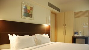Habitación de hotel con una cama grande, un cabecero, una obra de arte enmarcada en la pared y una mesita con una tetera y botellas de agua.