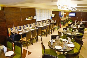 En moderne restaurant med flere spiseområder, herunder et aflangt fællesskabsbord og adskillige runde borde.