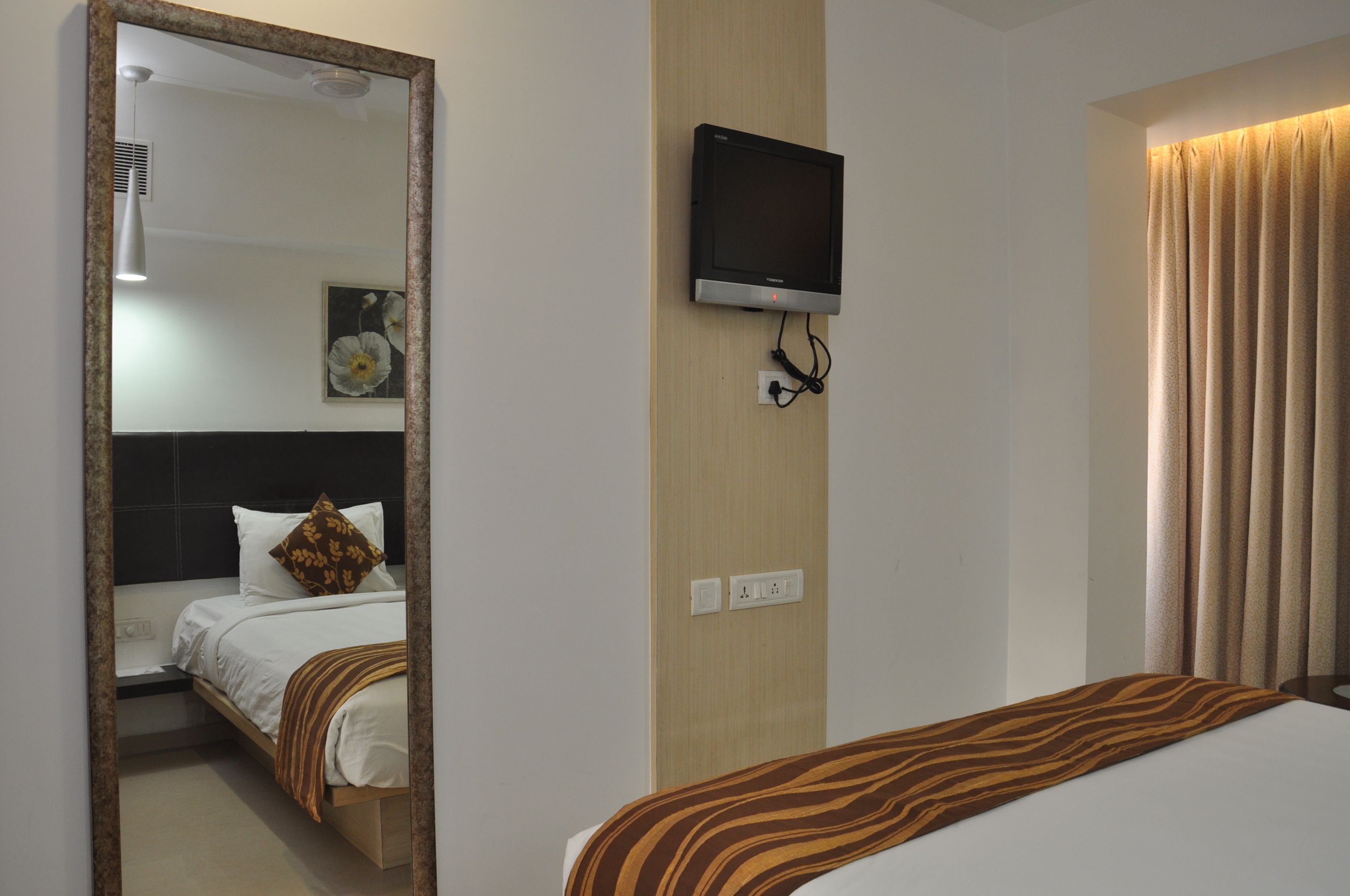 Ein Hotelzimmer mit Bett, Wandfernseher, Spiegel und einem Fenster mit Vorhängen.