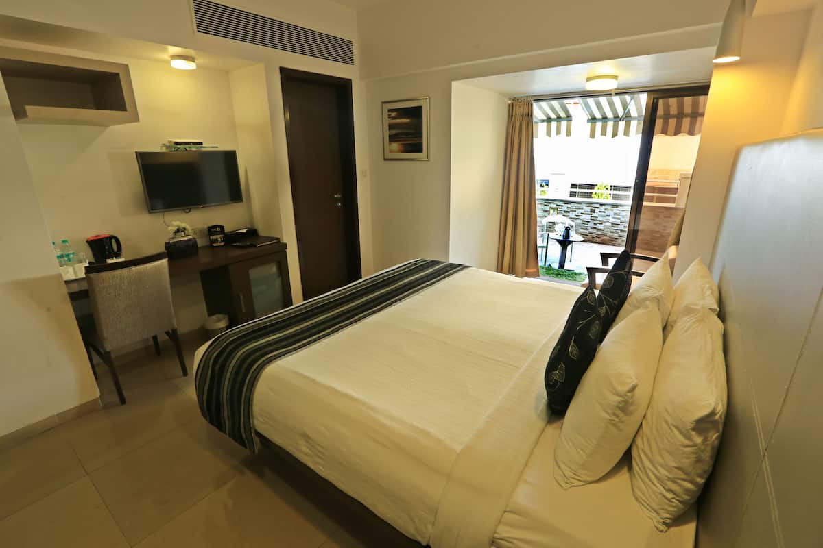 Habitación de hotel con cama, televisor, escritorio y silla, y ventana con cortinas.