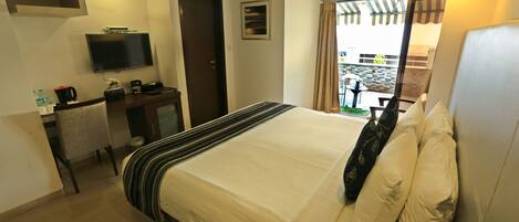 A hotel room with a bed, a TV, a desk with a chair, and a window with curtains.