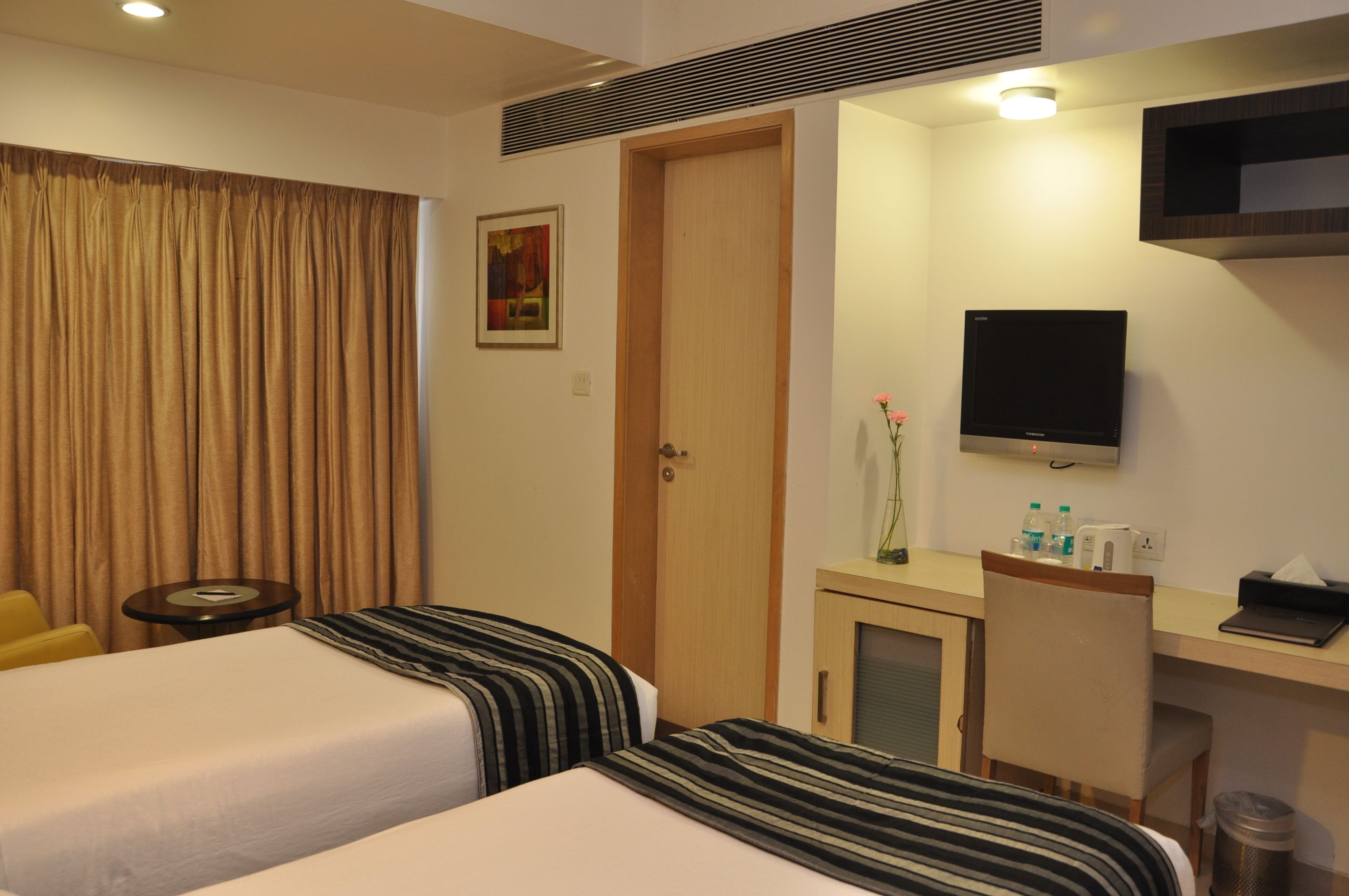 Une chambre d’hôtel avec deux lits, un bureau, une télévision, une petite table et une porte.