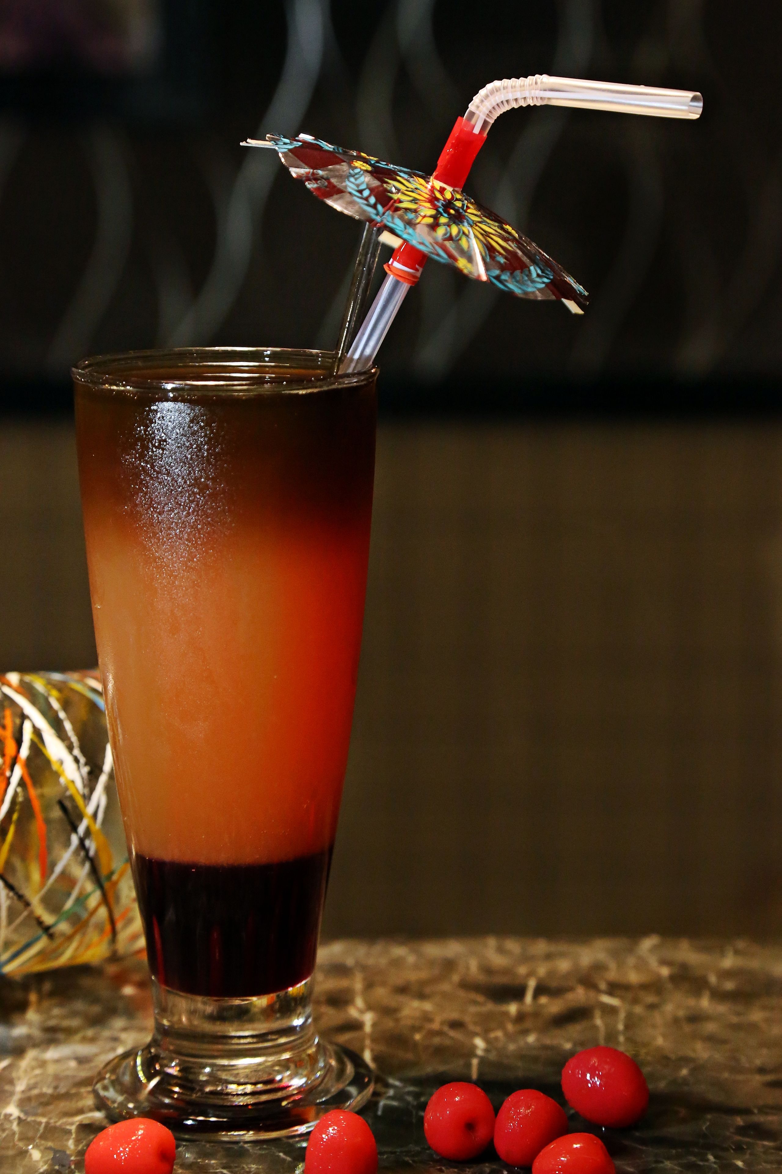 A tall glass with a gradient drink, a straw, and a decorative umbrella.