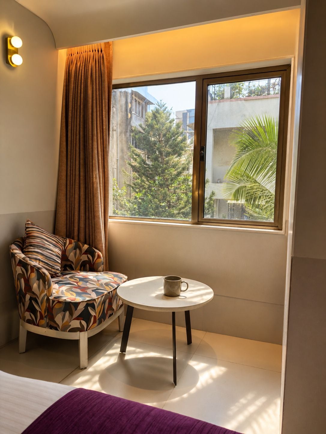 A corner room with a sofa, a small table, and a window with a view of buildings and trees.