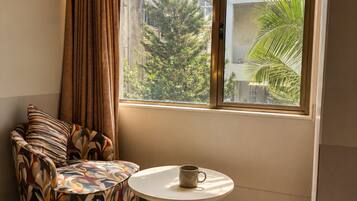 A corner room with a sofa, a small table, and a window with a view of buildings and trees.