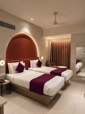 Une chambre d’hôtel avec un grand lit, une table de chevet, une chaise, une table ronde et un ventilateur de plafond.