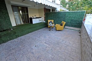 En terrasse med spisebord og gule stole, et lille rundt bord med en vase, og en grøn hækwall.