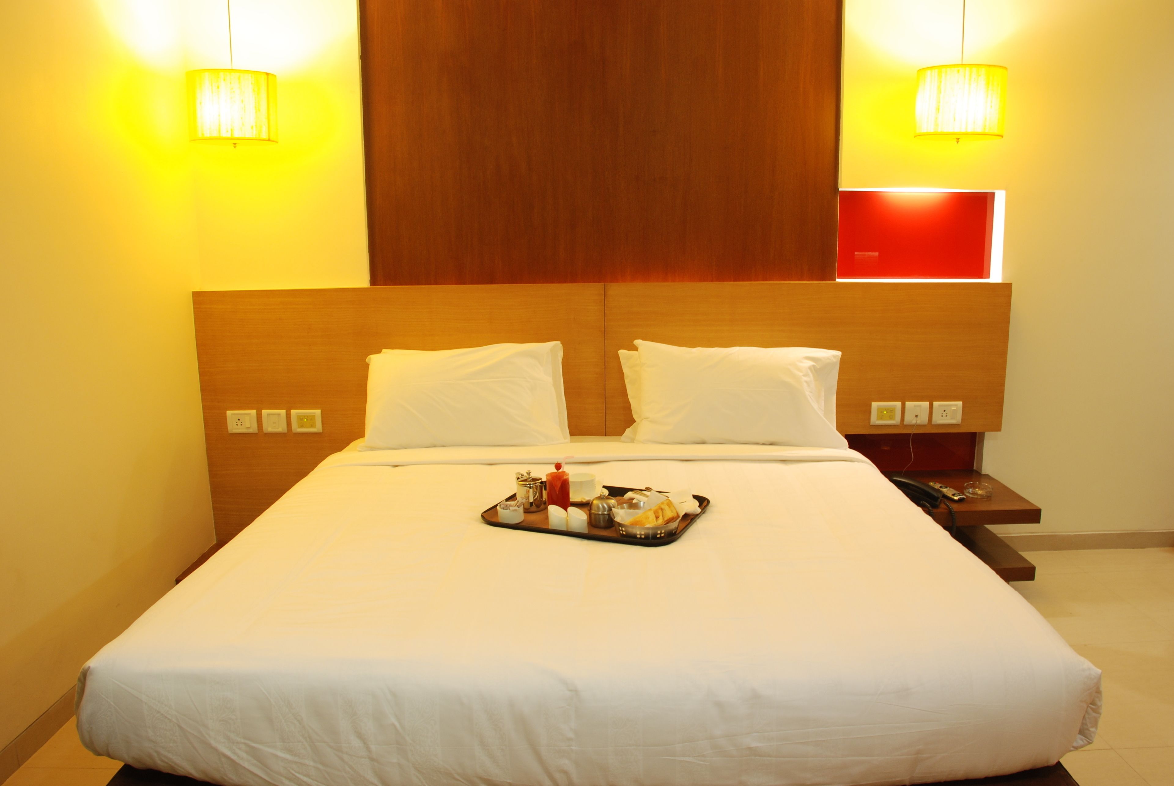 A hotel room with a large bed, two bedside lamps, a tray with breakfast items, and a red accent wall.
