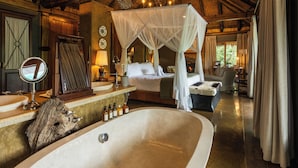 A spacious bedroom with a large bathtub, a canopy bed, and a rustic wooden ceiling.