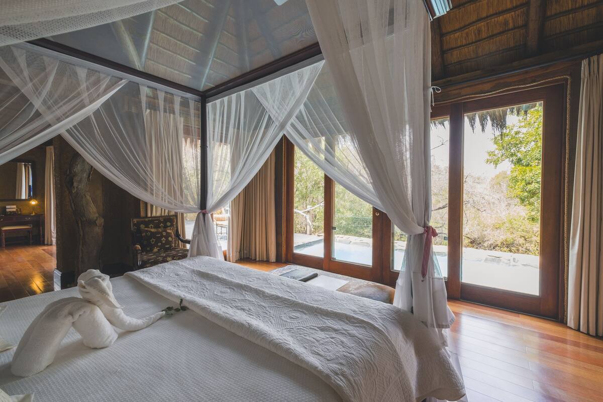 Un dormitorio con cama, cortinas blancas y vistas al exterior.