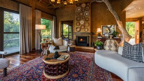 A spacious living room with a fireplace, large windows, and a chandelier.