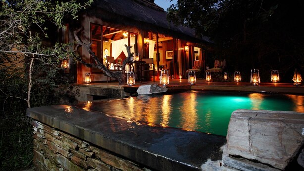 A thatched-roof building with a pool, stone walls, and lanterns.