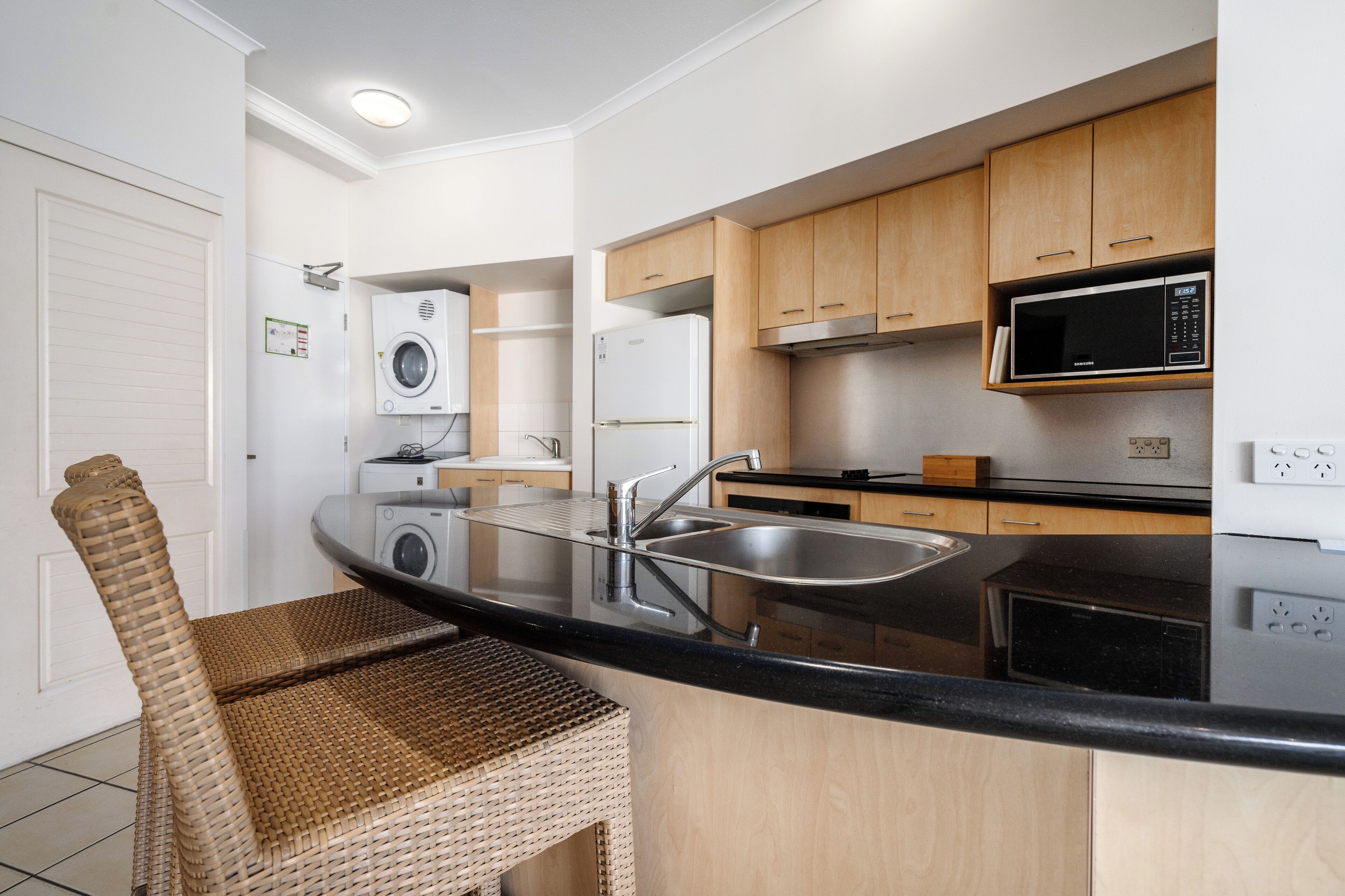 A modern kitchen with a built-in washing machine, a microwave, and a stainless steel sink.