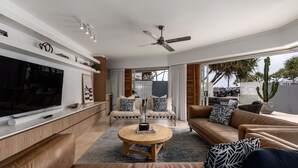 Een moderne woonkamer met een flatscreen televisie, leren banken, een ronde salontafel en een plafondventilator.