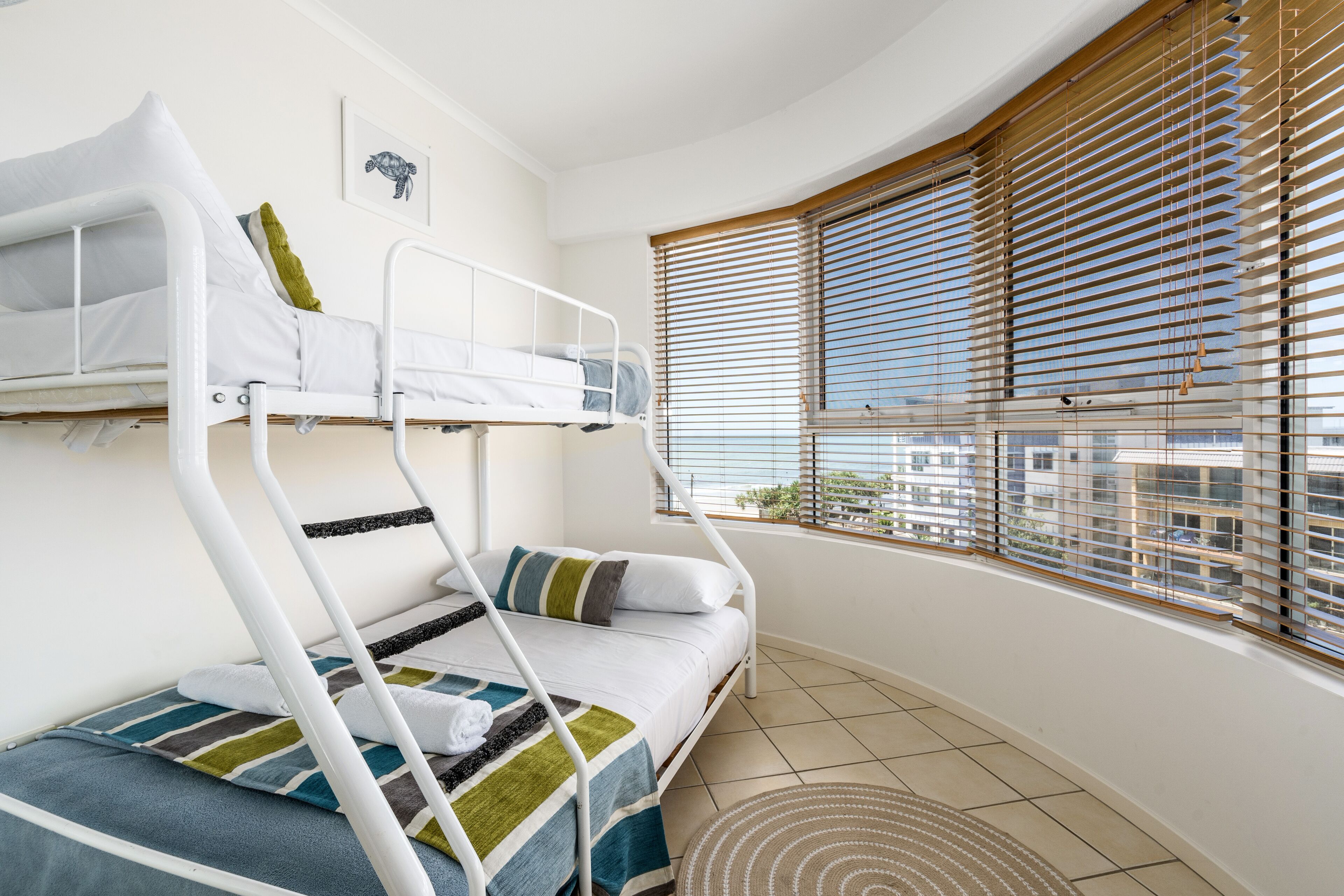 Een slaapkamer met stapelbedden en uitzicht op de stad door grote ramen met zonwering.