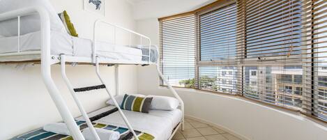 A bunk bed room with a view of the city through large windows with blinds.