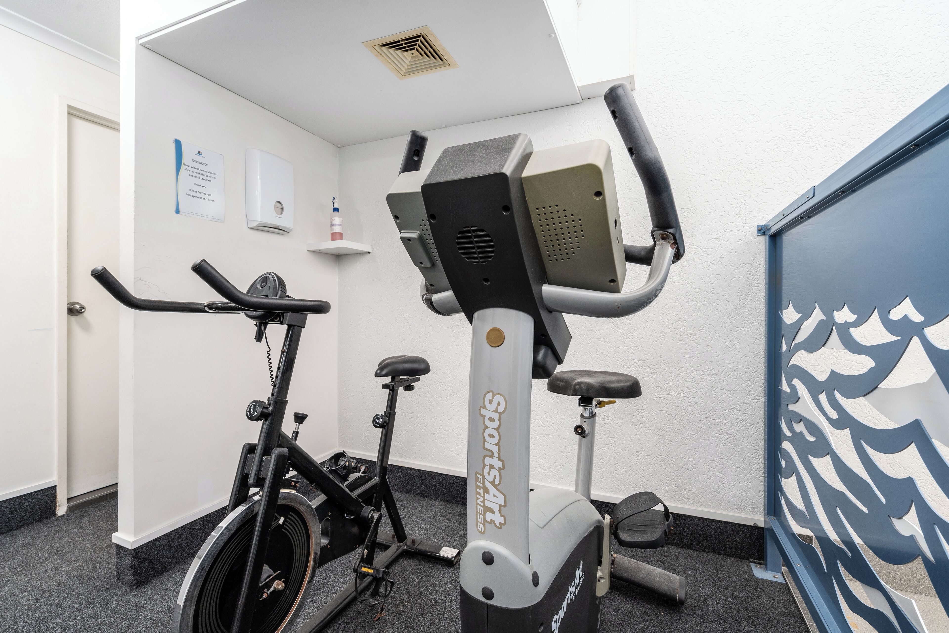 A fitness room with two stationary bikes, a water dispenser, and a wall-mounted sign.