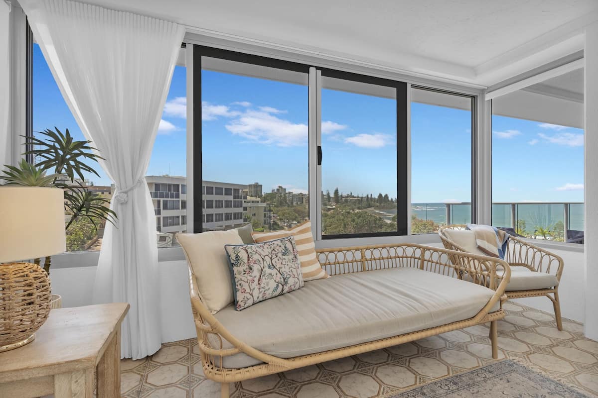A balcony with wicker furniture, a view of the city, and a clear sky.