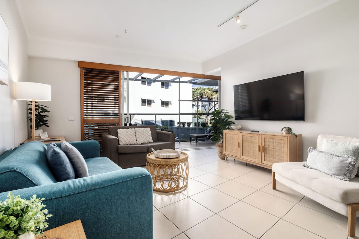 A modern living room with a teal sofa, a white sofa, and a television mounted on the wall.