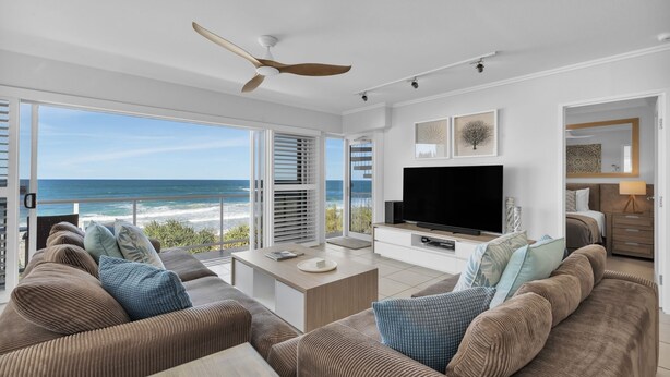 Een moderne woonkamer met een grote televisie, comfortabele zitplaatsen en uitzicht op de oceaan.