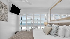 Een moderne hotelkamer met een groot bed, een flatscreen televisie aan de muur en een groot raam met witte jaloezieën.