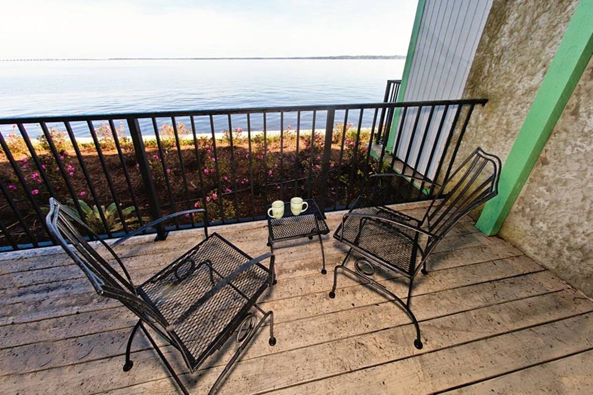 A balcony with metal chairs and a small table, overlooking a body of water with flowers in the background.