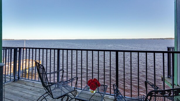 A balcony with a view of the water, a table with a vase of flowers, and two chairs.