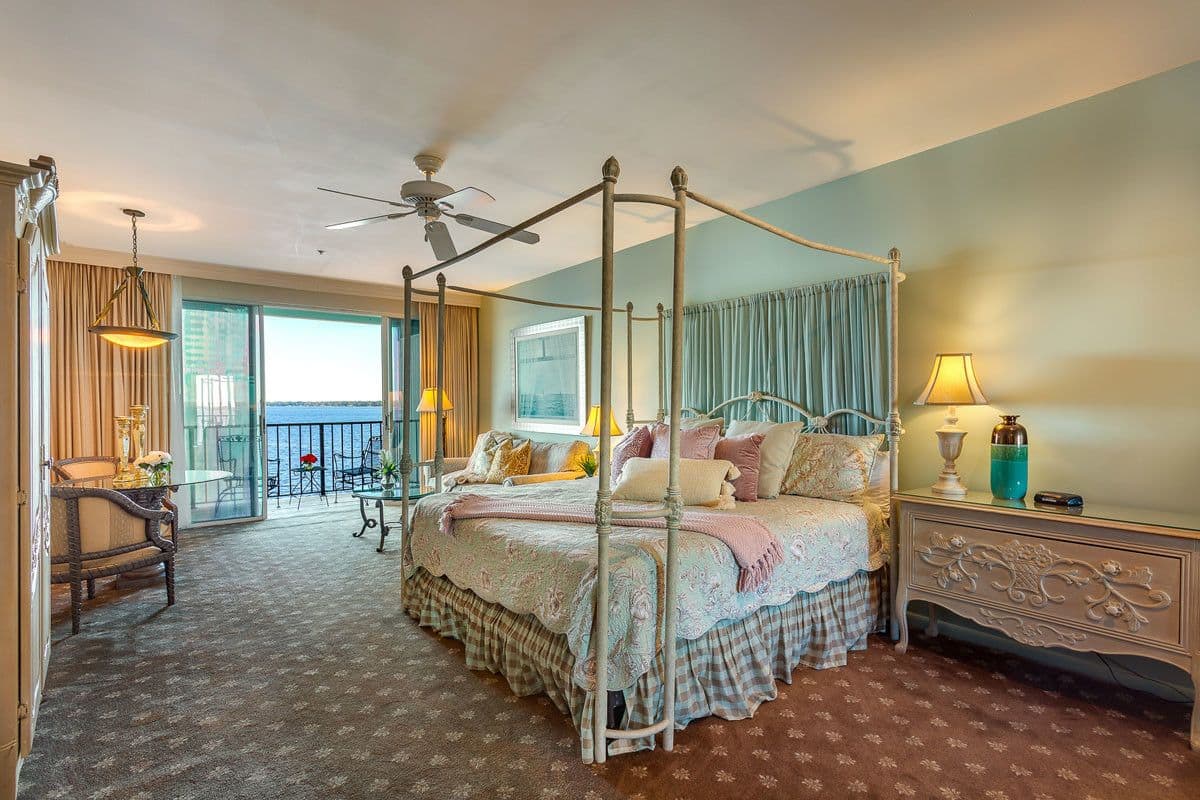 A four-poster bed with a canopy, a balcony with a view, and a dining area with a table and chairs.