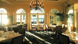 A dining area with tables set for a meal, large windows with a view, and a chandelier.