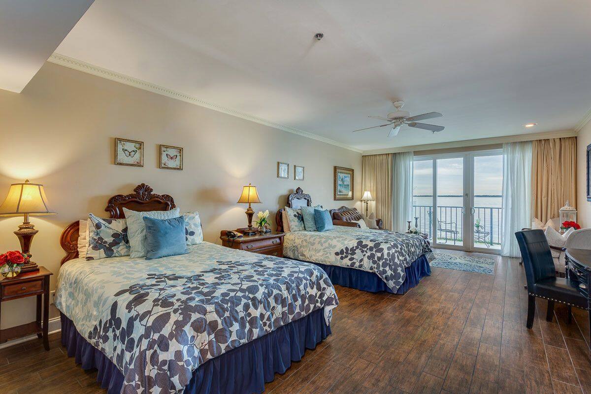 A hotel room with two beds, a ceiling fan, a balcony with a view, and a dining area.