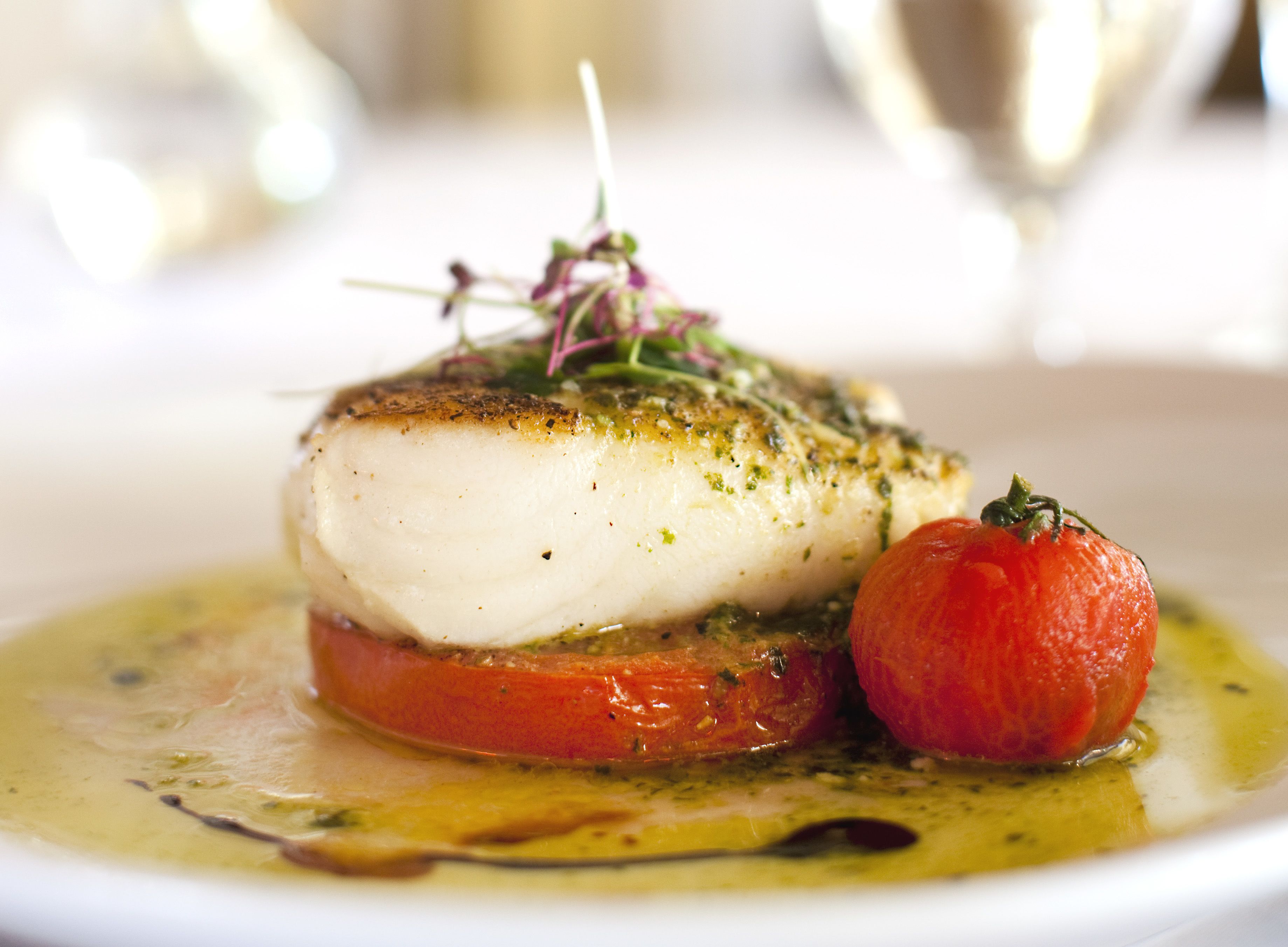 A dish of fish with a tomato and a garnish on a plate.