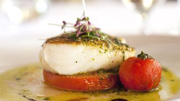 A dish of fish with a tomato and a garnish on a plate.