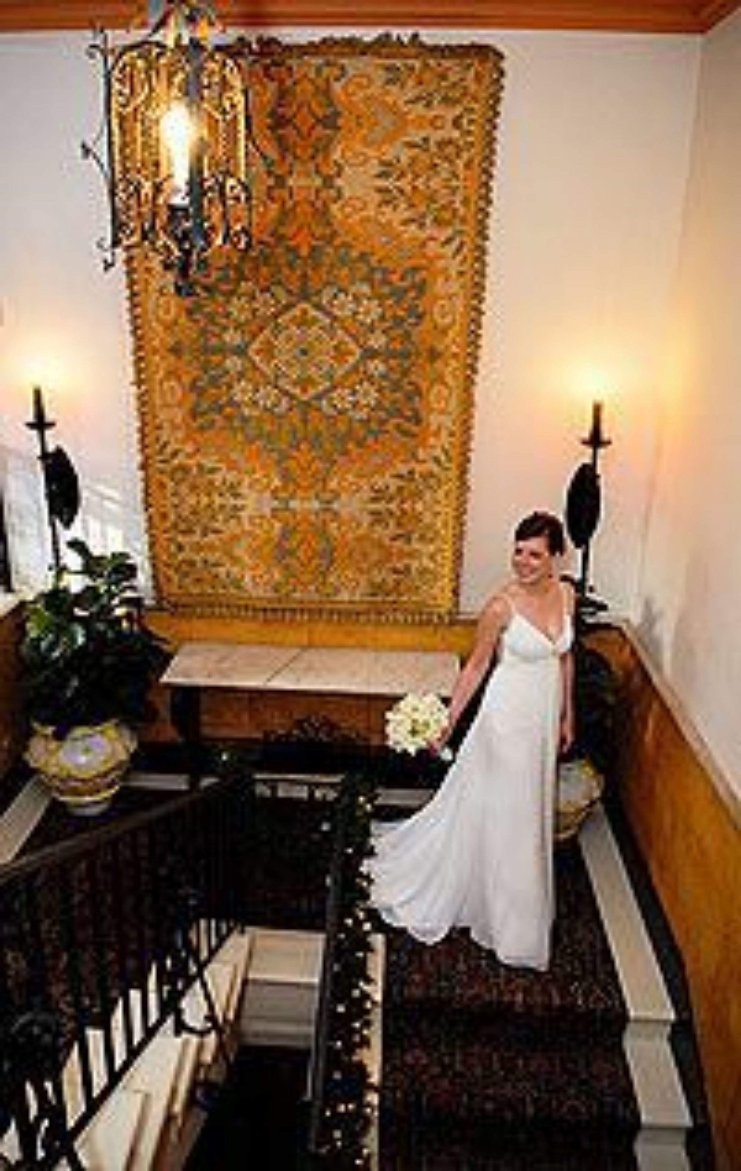 A staircase with a patterned carpet, a chandelier, and a person in a white dress.