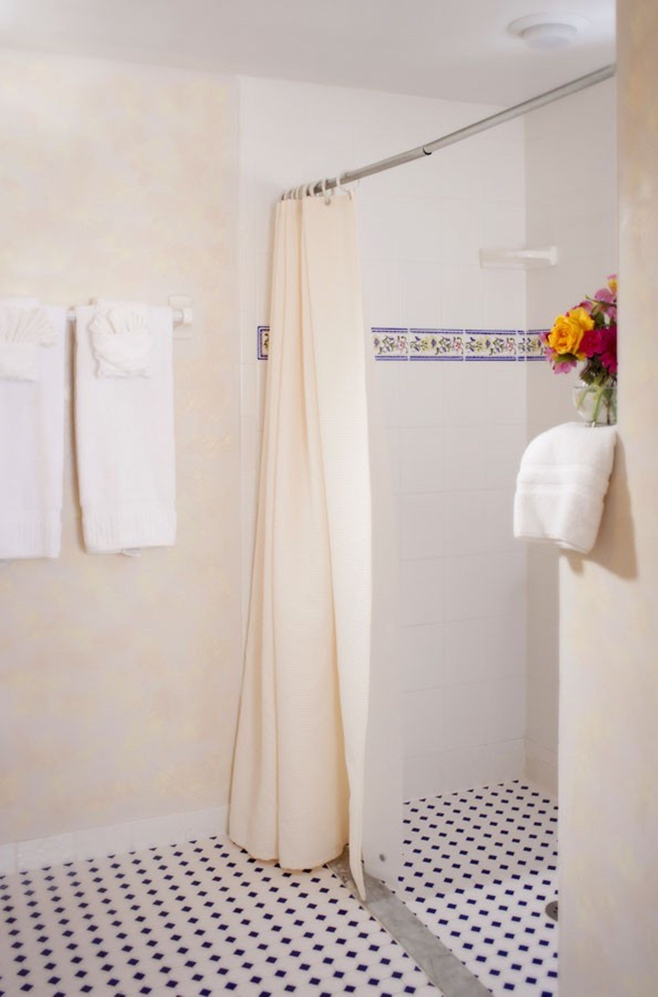 A shower with a beige curtain, a white towel rack with towels, and a patterned floor.