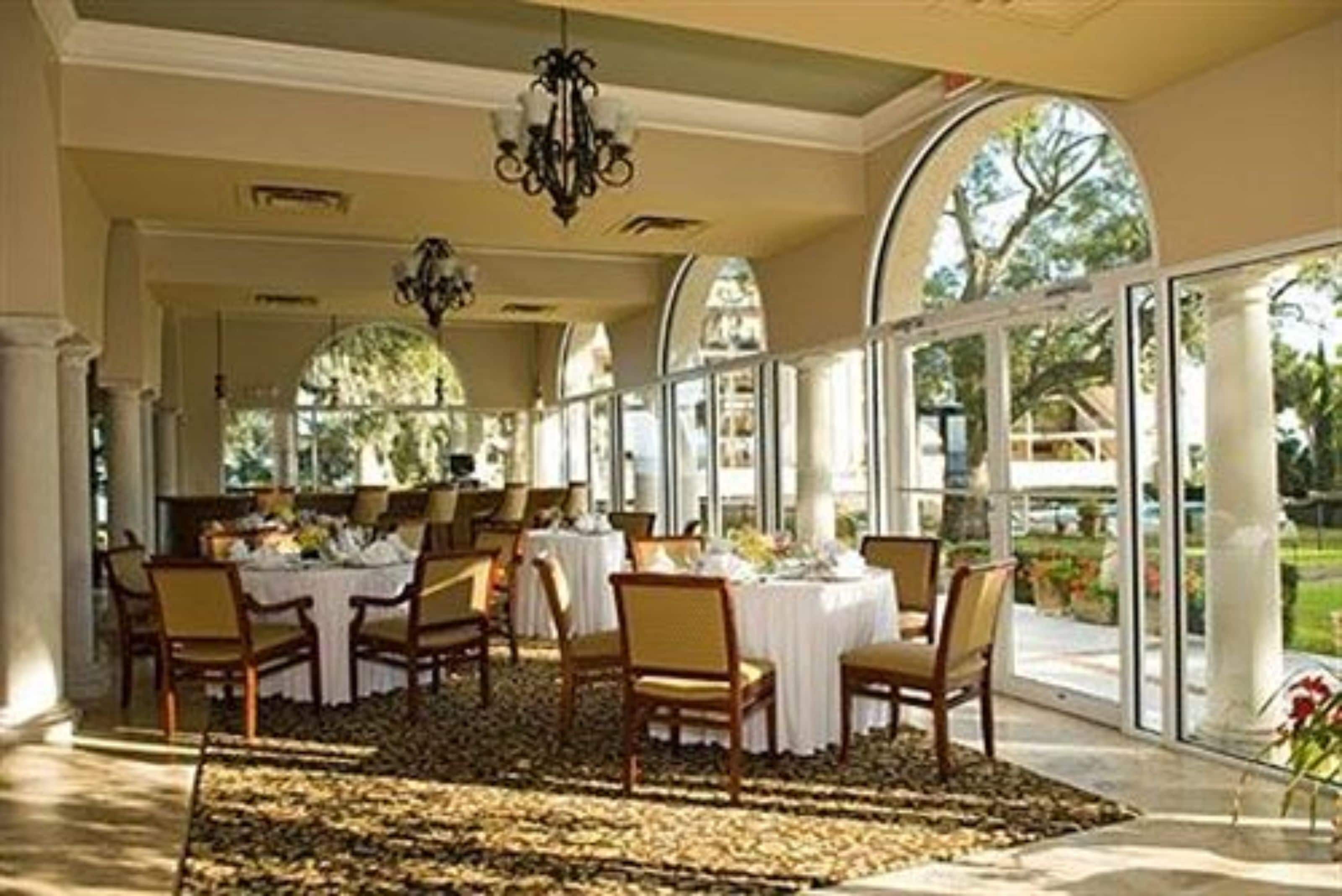 Un comedor con mesas redondas, sillas y un candelabro.