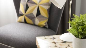 A modern room with a grey sofa, a geometric patterned pillow, a white desk lamp, and a potted plant on a wooden and glass table.