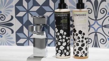 Two bottles of Cow Shed hand cream and a Vessini faucet on a bathroom sink.