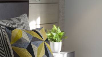 Cama bem arrumada com almofadas estampadas, abajur e planta em vaso.