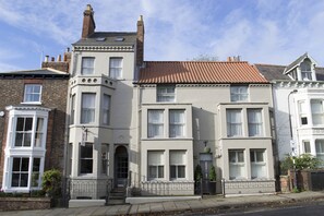 A row of white terraced houses with a brick chimney, a small garden, and a metal fence. - Jorvik House (York)