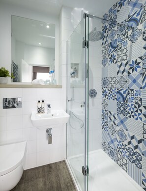 A modern bathroom with a glass-enclosed shower, a white sink, and a mirror above it. - Jorvik House (York)