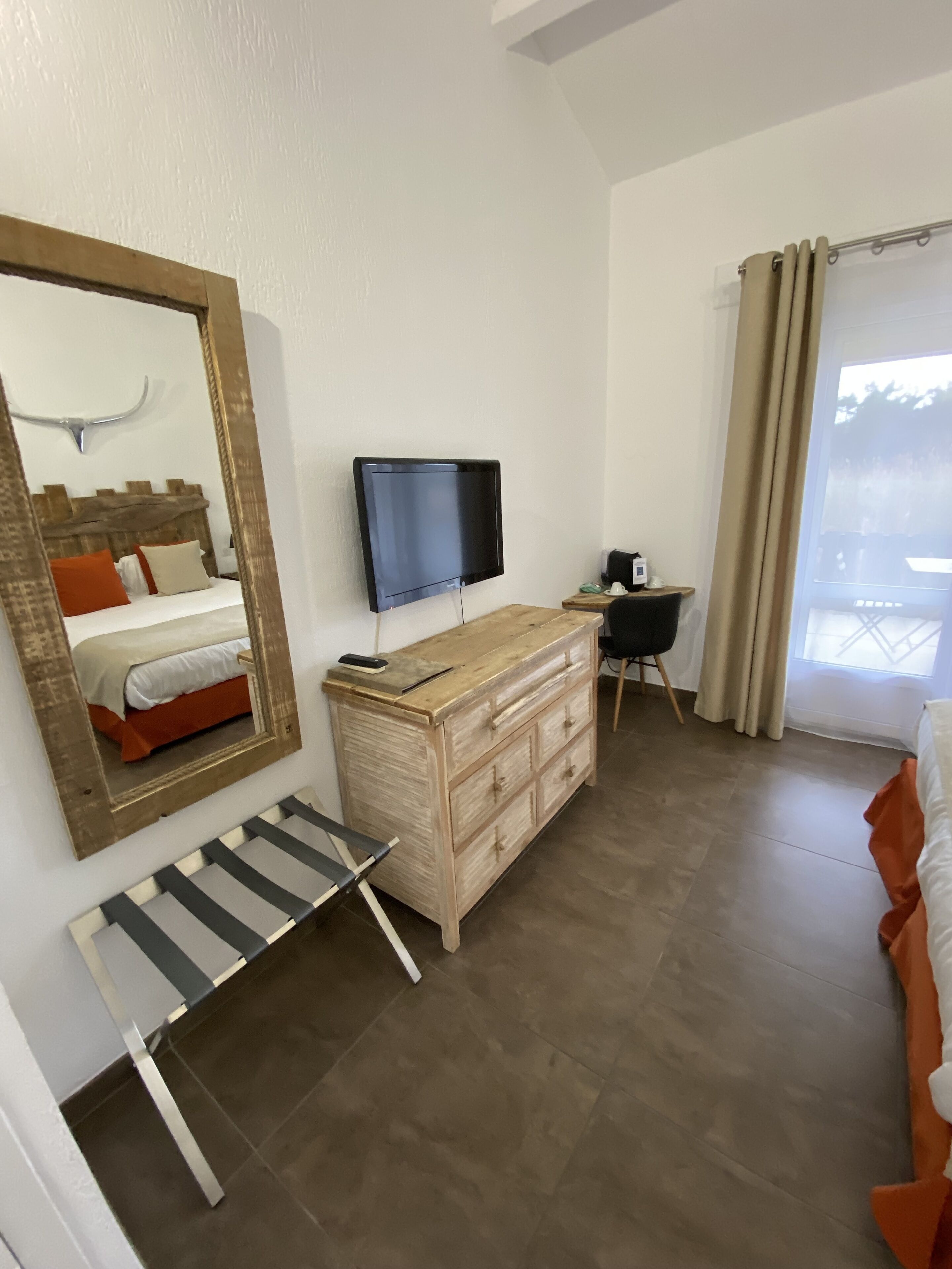 Habitación de hotel con tocador de madera, televisor montado en la pared, cama con ropa de cama naranja, un banco y un espejo grande.