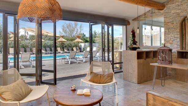 Espaço moderno em ambientes internos com vista para piscina, cadeiras de descanso e uma mesa de madeira com um livro aberto.