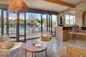 Een moderne binnenruimte met uitzicht op een zwembad, lounge stoelen en een houten tafel met een open boek.
