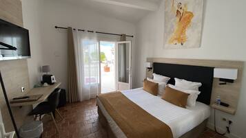 A hotel room with a bed, desk, chair, and a painting on the wall.