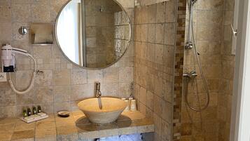 A bathroom with a stone sink, a round mirror, a handheld showerhead, and a towel rack.