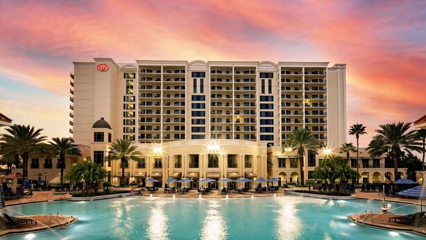 Un hotel con una piscina grande, varios balcones y palmeras.