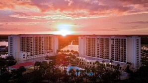 Un hotel con una piscina grande, varias edificaciones y una puesta de sol al fondo.