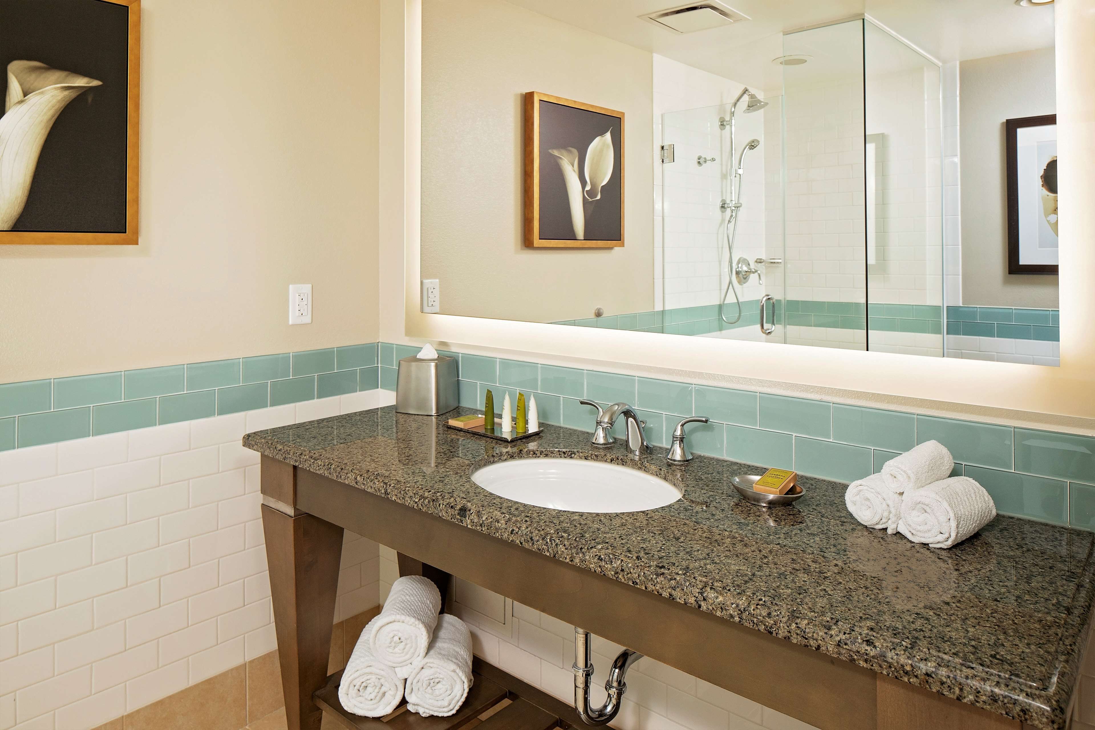A bathroom with a granite countertop, white sink, and a glass-enclosed shower. There are towels and toiletries on the counter.