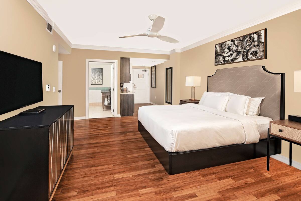 Ein modernes Hotelzimmer mit einem großen Bett, einem Flachbildfernseher, einem Deckenventilator und einem Gemälde an der Wand.