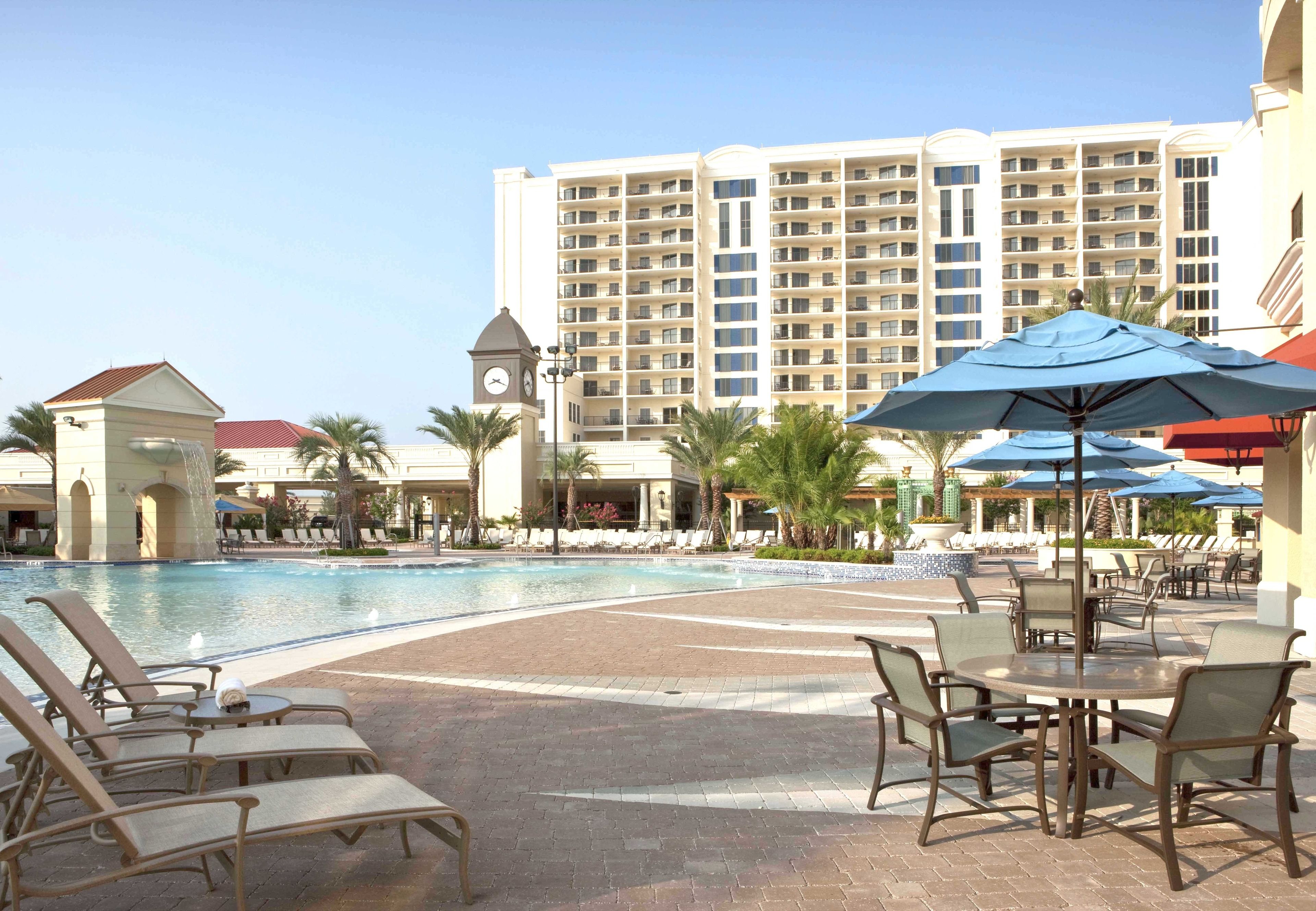 A hotel pool area with lounge chairs, umbrellas, and a clock tower.